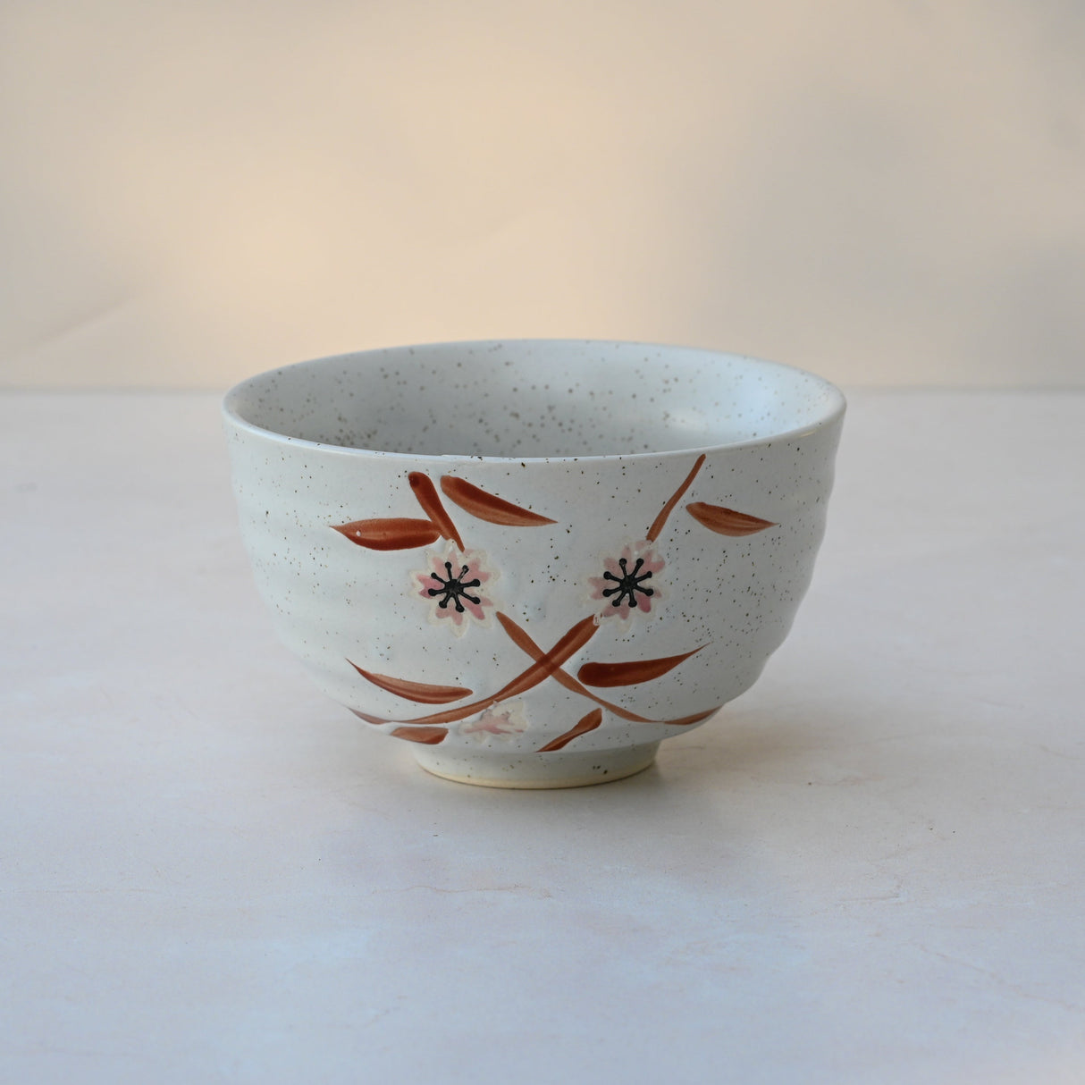 The Bamboo Matcha Bowl, featuring a floral white ceramic design in red and black, sits on a light surface. It's perfect for complementing the Bamboo Matcha Whisk and Whisk Holder Set.