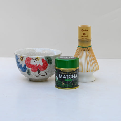 The Red and Blue Flowers Matcha Bowl, along with a bamboo matcha whisk and whisk holder set, rests elegantly on a white surface.