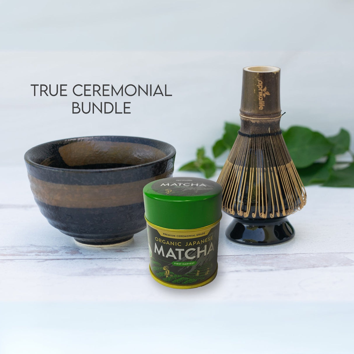 The Dark Brown Glaze Ceramic Matcha Bowl set includes a bamboo matcha whisk, whisk holder, and organic Japanese matcha, displayed on a white surface.