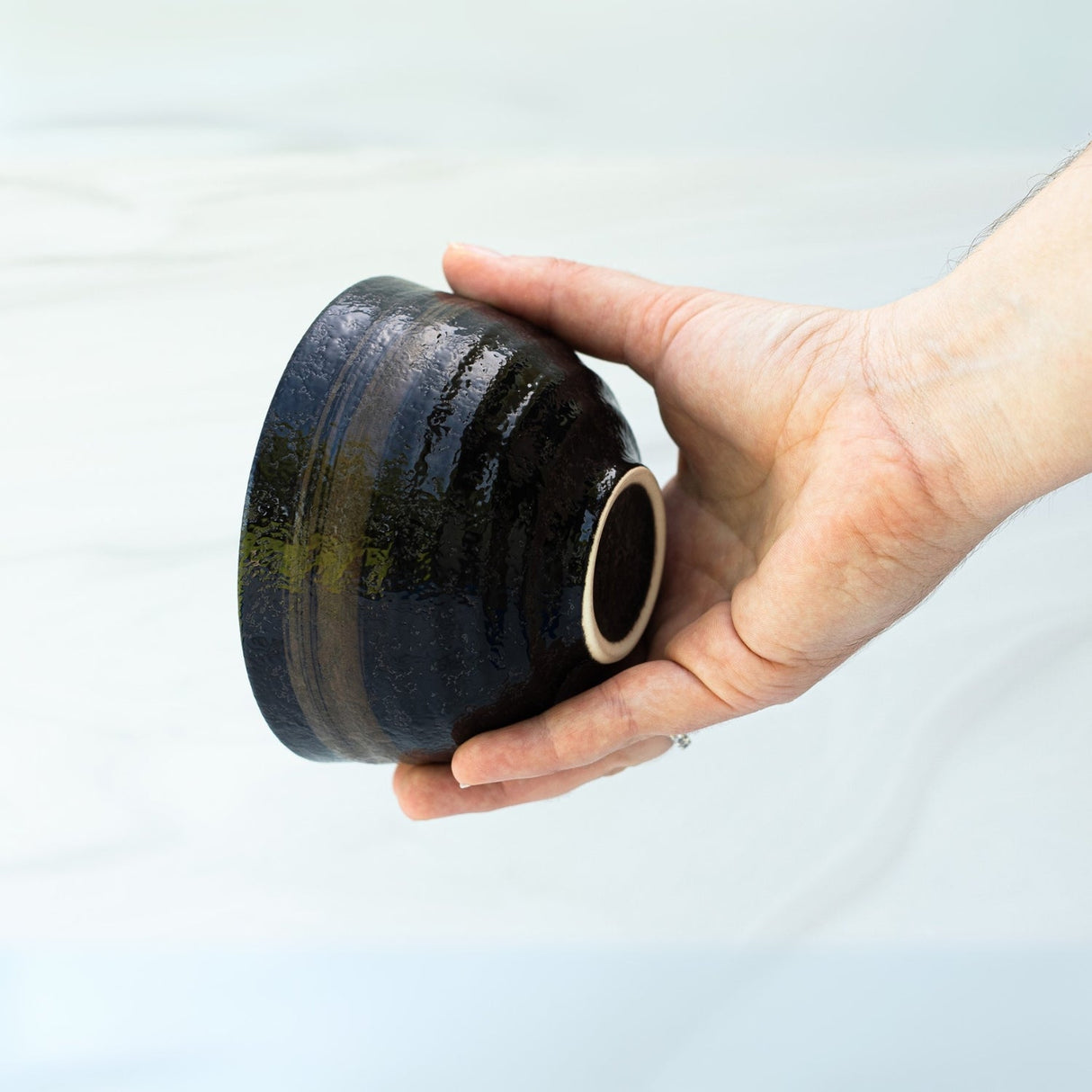 A hand holds a Dark Brown Glaze Ceramic Matcha Bowl with a textured surface against a light background, expertly crafted using traditional Minoyaki techniques.