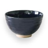 The Dark Navy Blue Ceramic Matcha Bowl, with its glossy finish and light-textured base, sits elegantly on a black background, making it perfect for any matcha tea starter set.