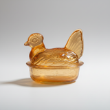 Amber-colored glass container shaped like a chicken on a white background