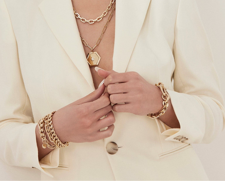 Person wearing gold jewelry including a necklace, bracelet, and ring on a light background
