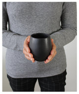 Person holding a black ceramic cup against a neutral background