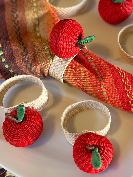 Napkin rings with red apple designs on a decorative tablecloth.