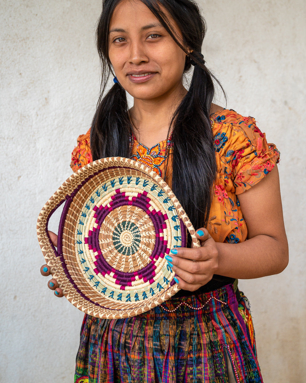 Woman holding a colorful woven basket against a plain background