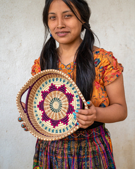 Woman holding a colorful woven basket against a plain background