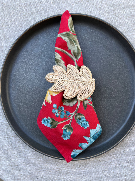 Decorative leaf napkin ring on a floral-patterned fabric on a black plate.