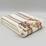 Beige blanket with colorful striped pattern and tassels on a white background