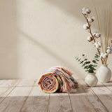Colorful woven mat on a wooden floor with decorative plants against a beige wall.