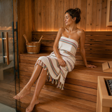 Woman sitting in a sauna with a striped towel draped over her shoulders.