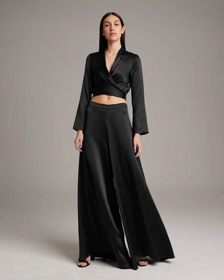 Woman wearing a black outfit with a long skirt and top on a plain background