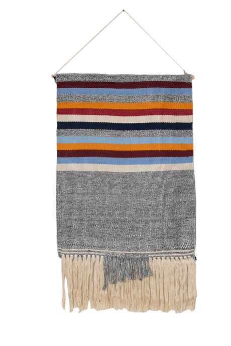 Woven wall hanging with colorful stripes and fringes on a white background