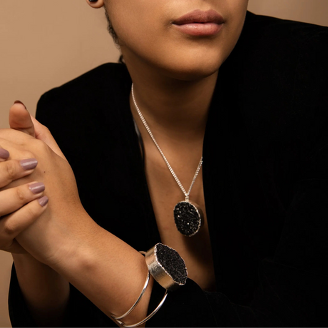 Person wearing a black druzy pendant necklace and bracelet on a neutral background