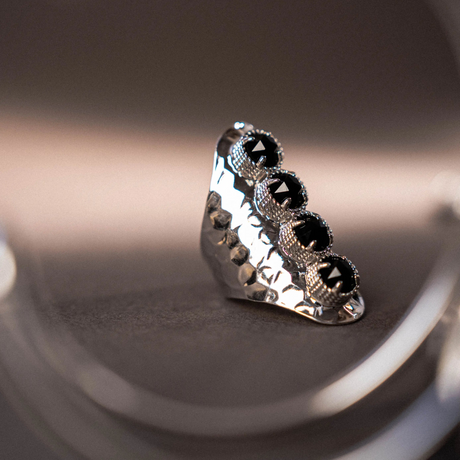Silver ring with black gemstones on a reflective surface