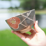 A hand holds the Gray with Flowers Ceramic Matcha Bowl from the Organic Japanese Matcha Set, set against a blurred outdoor background.