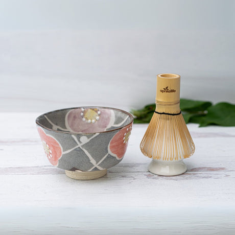Gray ceramic matcha bowl with a floral design and bamboo whisk from the Japanese matcha set, displayed on a white surface.