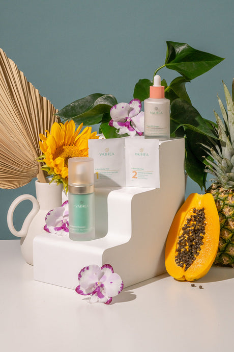 Cosmetic products on a white stand with decorative elements like flowers and a pineapple.