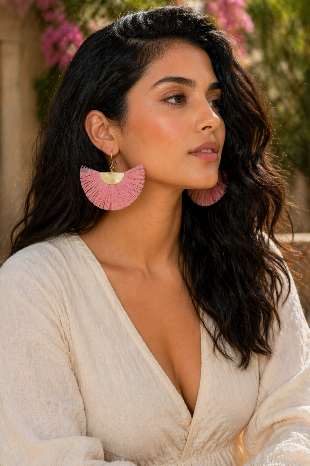 Woman wearing pink ruffled earrings with a blurred outdoor background