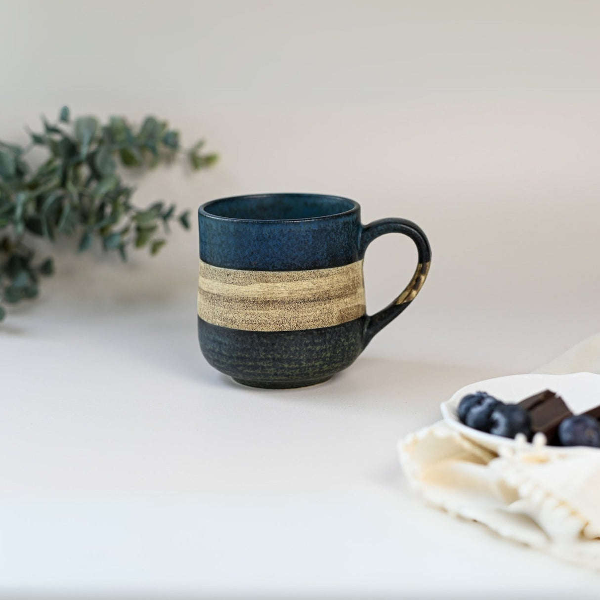 A Handcrafted Mino Ware Ceramic Mug from Japan (8 oz, blue and beige) sits on a table next to grapes and a white cloth.