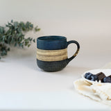 A Handcrafted Mino Ware Ceramic Mug from Japan (8 oz, blue and beige) sits on a table next to grapes and a white cloth.