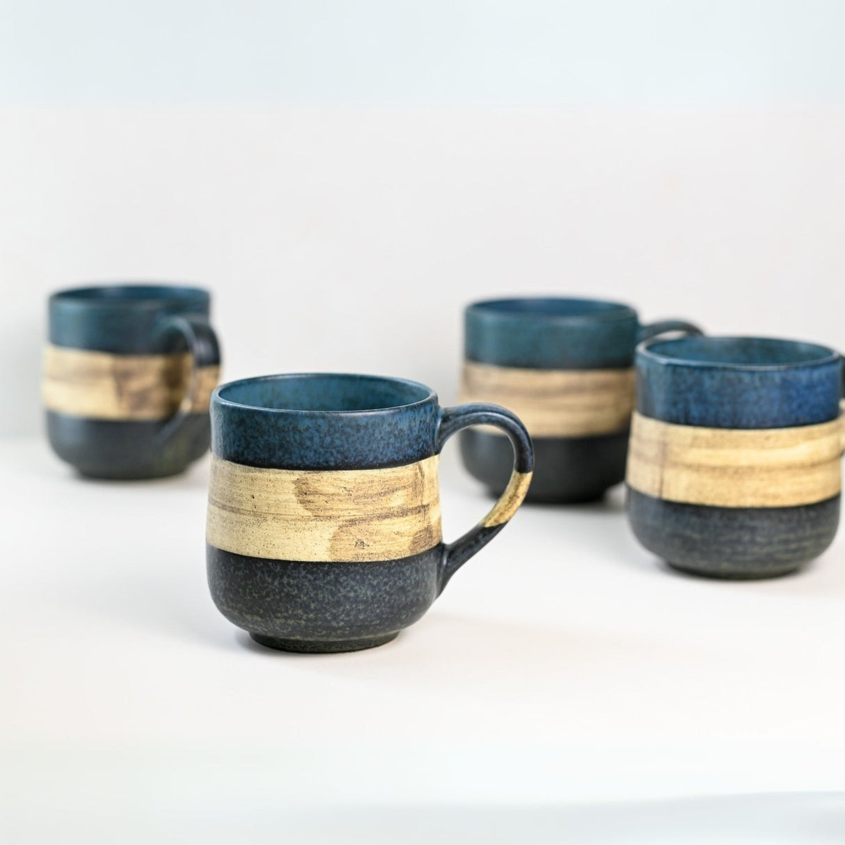 Four Handcrafted Mino Ware Ceramic Mugs from Japan, each 8 oz (240 ml), featuring blue and beige bands, are displayed elegantly on a white surface, embodying the timeless artistry of Japanese pottery.