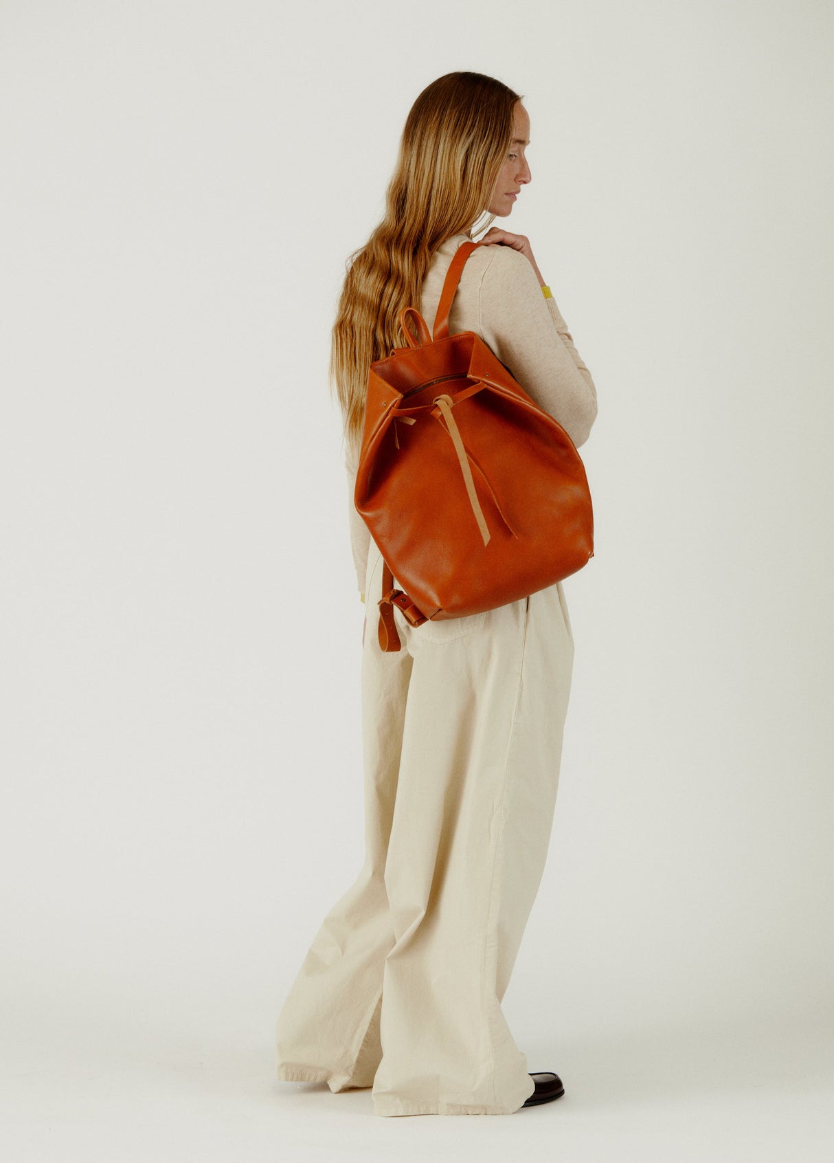 Person holding a brown leather backpack against a white background