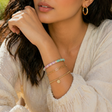 Close-up of a person wearing multiple bracelets on their wrist with a blurred natural background