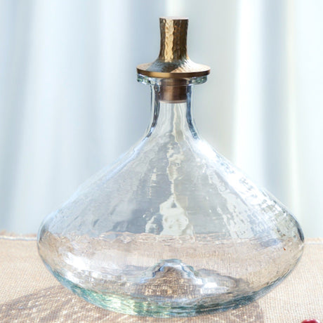 Clear glass decanter with a cork stopper on a light surface with a blurred background