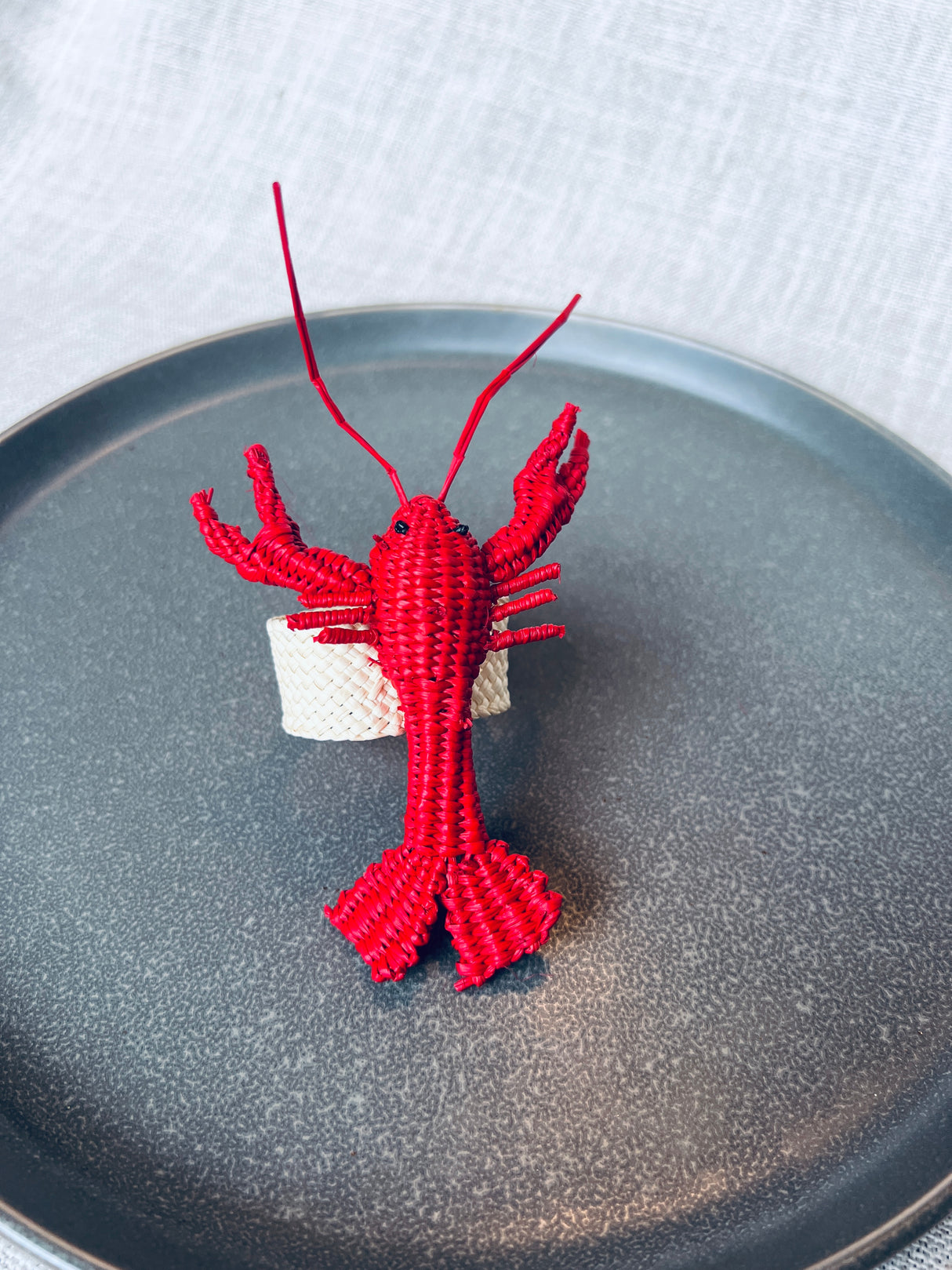 Red lobster-shaped napkin ring on a gray plate with a white background