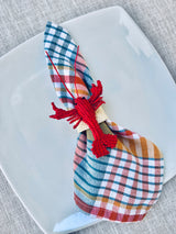 Plaid napkin with a red lobster napkin holder on a white plate.