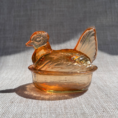 Amber glass hen-shaped container on a textured surface