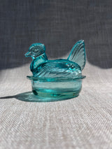 Turquoise glass hen-shaped object on a textured surface