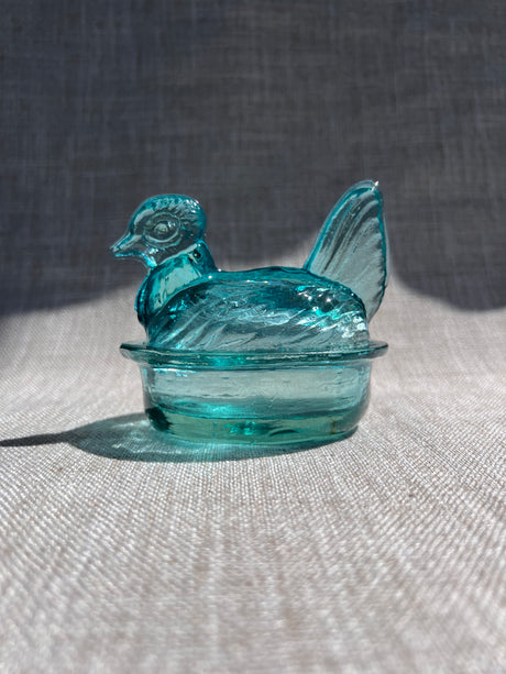 Turquoise glass hen-shaped object on a textured surface
