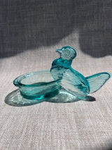 Turquoise glass hen figurine on a textured fabric background