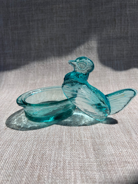 Turquoise glass hen figurine on a textured fabric background