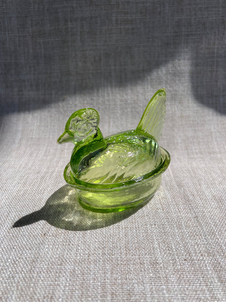 Green glass nesting hen bowl on a textured gray surface