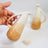 Hand holding a gradient ceramic pitcher with another pitcher in the background on a white surface.