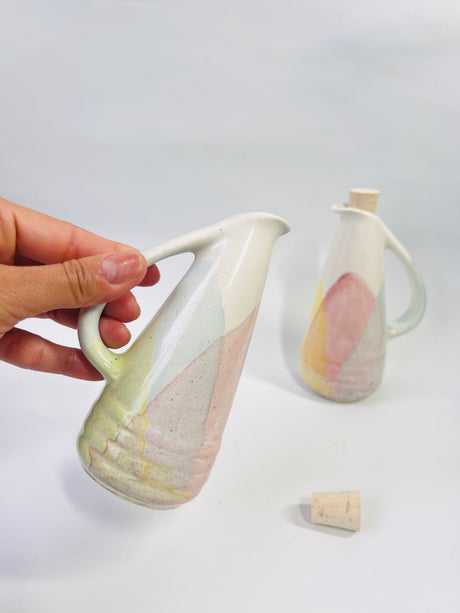 Hand holding a ceramic pitcher with a second pitcher in the background on a white surface