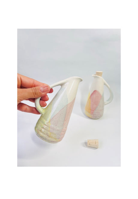 Ceramic pitcher with a hand holding it on a light gray background