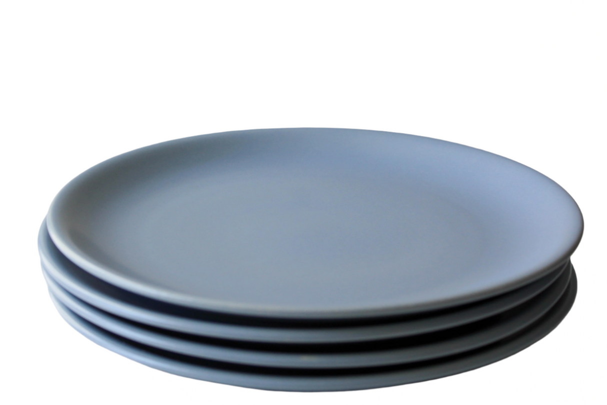 A green ceramic dinner plate with a yellow and red decorative element, placed on a stack of three plates of the same color.
