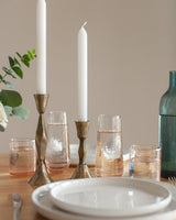 Dining table setting with candles, glasses, and a bottle on a neutral background