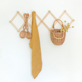 Wall-mounted wooden hook rack with a yellow cloth, basket, and decorative items on a white background