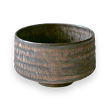 A rough-textured, dark gray ceramic bowl with a slightly metallic finish on a black background, highlighting craftsmanship similar to Japanese pottery, reminiscent of the Kaneni Gold Crystal Ceramic Matcha Bowl.