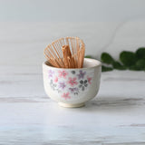 Kohiki Pink Sakura Ceramic Matcha Bowl with a bamboo matcha whisk set on a light wooden surface.