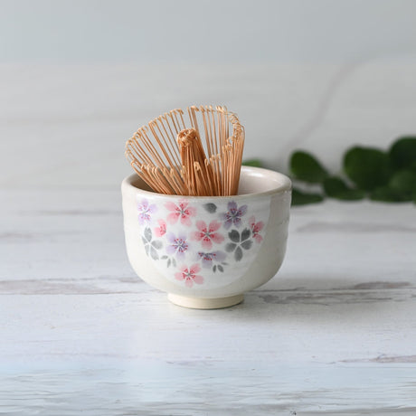 Kohiki Pink Sakura Ceramic Matcha Bowl with a bamboo matcha whisk set on a light wooden surface.