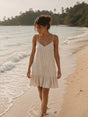 Woman in a striped dress walking on a beach with ocean waves and greenery in the background