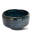 The Indigo Glaze Matcha Bowl, handcrafted in Japan, features a beautifully glossy, textured surface with an irregular rim. Its dark ceramic design enhances its appeal as a refined matcha tea accessory.