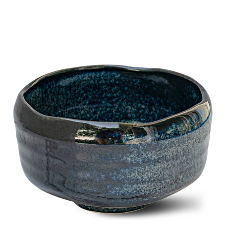 The Indigo Glaze Matcha Bowl, handcrafted in Japan, features a beautifully glossy, textured surface with an irregular rim. Its dark ceramic design enhances its appeal as a refined matcha tea accessory.