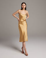 Woman wearing a gold slip dress against a plain background
